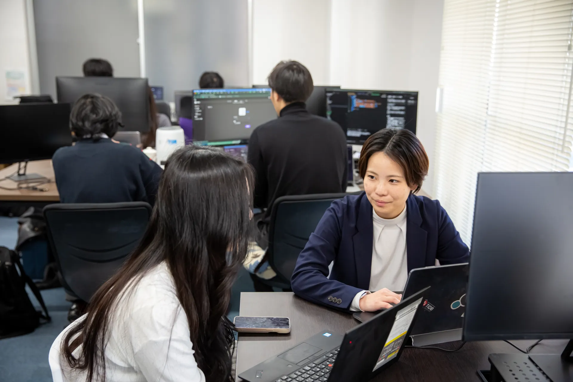 オフィスでノートパソコンを囲み、打ち合わせをする社員
