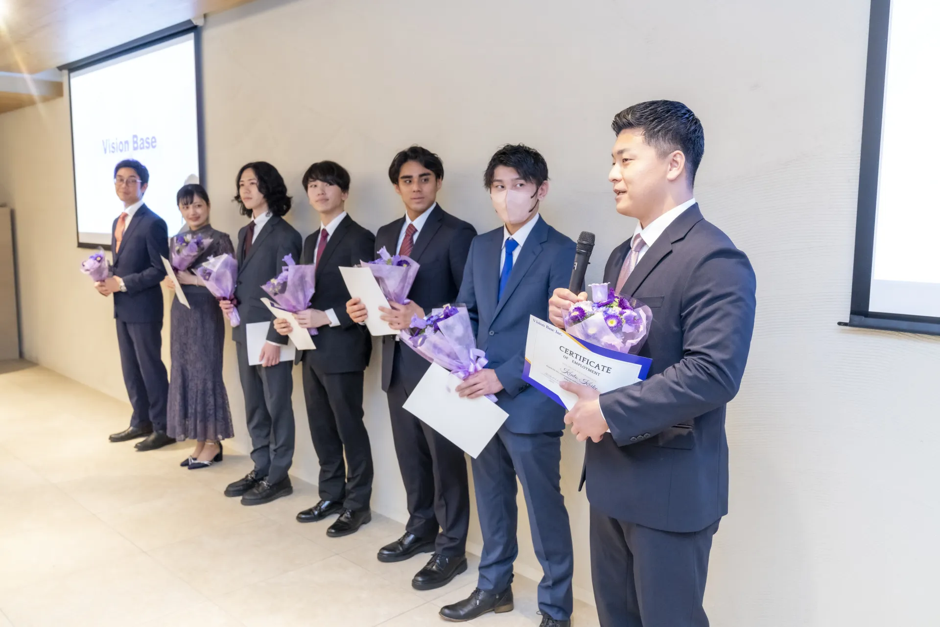 入社式で花束と辞令を手に並ぶ社員たち
